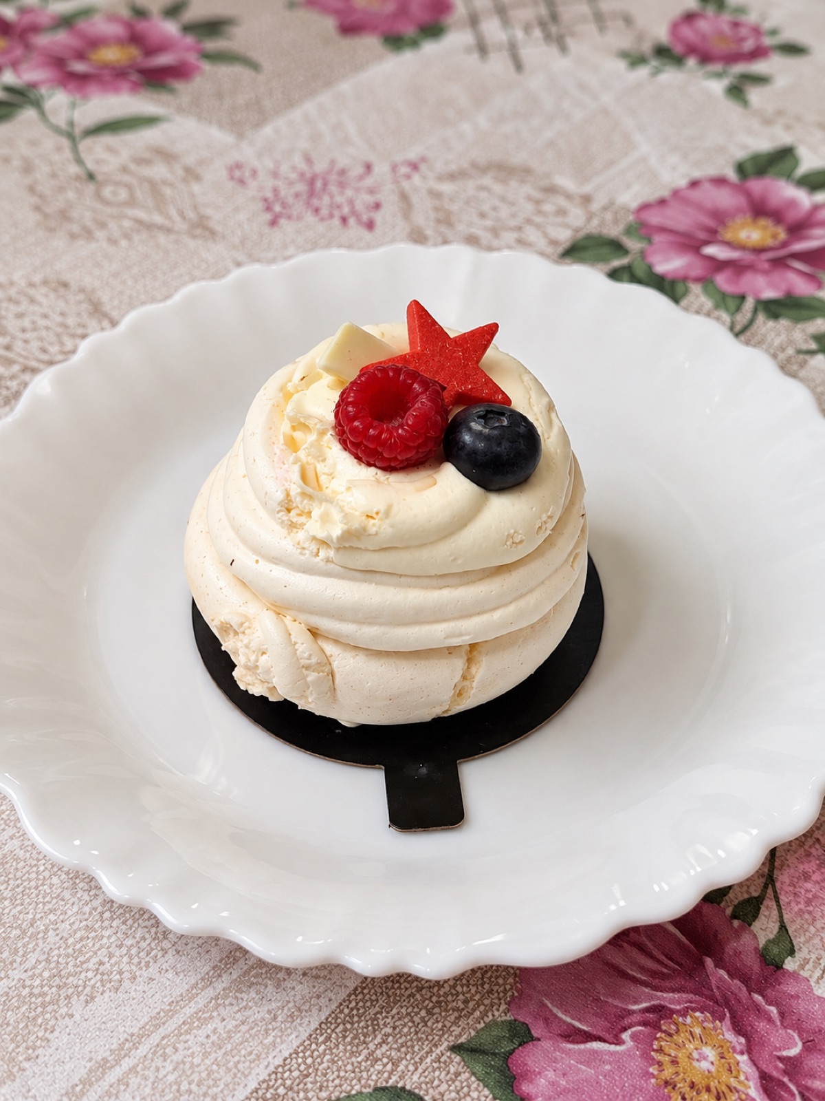 A meringue crowned with cream, a raspberry and a blueberry, on a scalloped plate